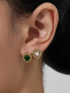 Close-up of heart earrings with green and clear stones in gold plating on model