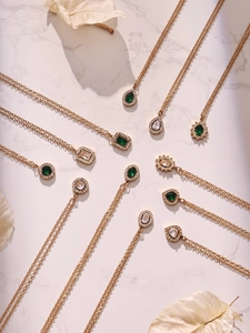 Flat lay of gold teardrop and geometric necklaces with emerald green zircons on marble