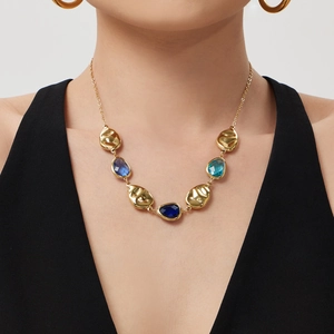 Gold hammered necklace with faceted blue teardrop stones worn by a model in neutral light