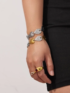Close-up of dual-tone leaf chain bracelet and ruby pearl ring on model in dark setting