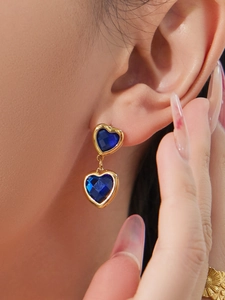 Gros plan de boucles d'oreilles cœur dorées avec pierres bleues portées par un mannequin