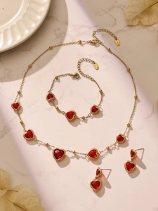 Détail d'une parure en acier doré avec pierres en verre en forme de cœur rouge