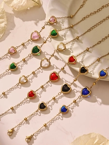 Détail de colliers de pierres précieuses en cœur avec chaînes à billes d'or sur marbre