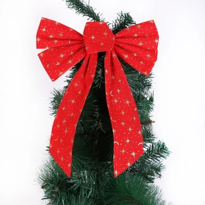Top view of a large red velvet Christmas bow with gold glitter stars on a green tree
