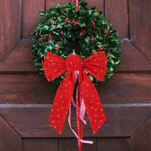 Red velvet Christmas bow with gold stars on a green holly wreath over a wooden door