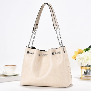 Minimalist beige bucket shoulder bag with chain strap detail on a lifestyle background