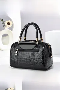 Detail of glossy black crocodile pattern texture and gold metal hardware on the bag