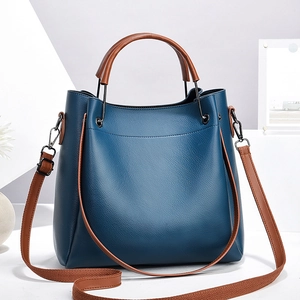 Sac seau en cuir bleu foncé avec poignées marron et bandoulière sur socle blanc