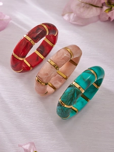 Detail of three marble resin bamboo bracelets with gold metal rings and floral decor