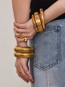Détail de bracelets et bagues dorés avec incrustation de zircon et texture ondulée
