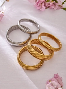 Gros plan de bracelets Tubogas en or 18k et argent empilés sur un tissu floral