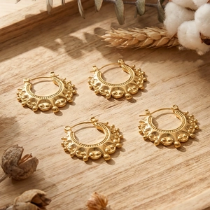 Golden bohemian gear earrings with beaded texture on a rustic wooden tray