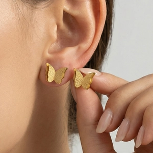 Golden butterfly stud earrings with matte texture shown worn on the earlobe