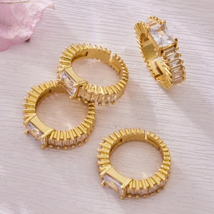Set of four gold plated rings with rectangular zircon stones on textured wooden background