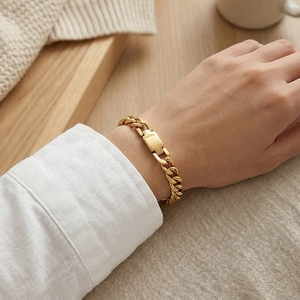 Polished gold Cuban link chain bracelet with a flat ID plate shown on a person's wrist