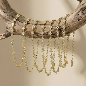 Gold-plated chain bracelet with blue enamel flowers hanging on a rustic wooden branch