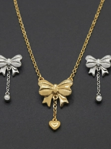 Macro shot of two-tone bow jewelry set including heart necklace and ball drop earrings