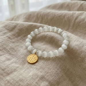 Cat eye stone bead bracelet with a golden Fu character charm on a textured linen background