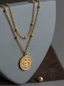Détail d'un collier double rang en or avec pendentif œil protecteur sur présentoir gris