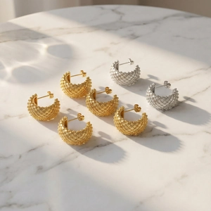 Golden and silver C-shaped mesh earrings with cross-woven texture on marble surface