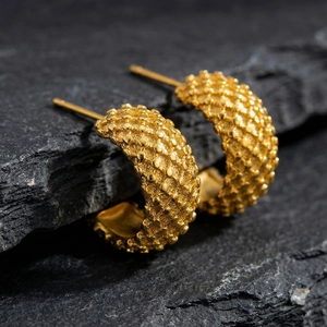 Golden C-shaped earrings with textured micro-beads on a natural stone background