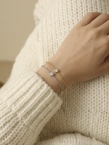 Nahaufnahme goldener und silberner Kettenarmbänder mit Zirkon auf weißem Pullover