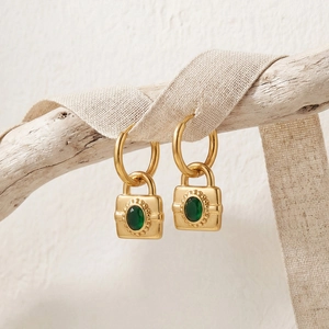 Boucles d'oreilles cadenas dorées avec zircon vert suspendues sur une branche rustique