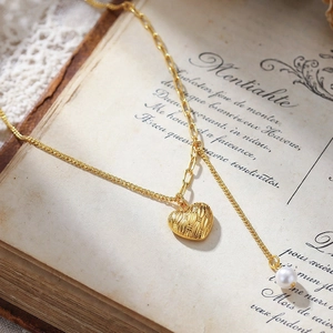 Collier élégant doré avec pendentif cœur tressé et perle sur des pages vintage