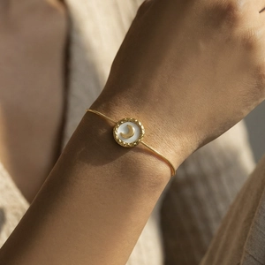 Golden snake chain bracelet with white shell moon pendant shown on female wrist