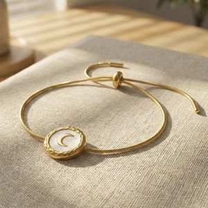 Gold moon charm snake chain bracelet with white shell inlay on linen textured background