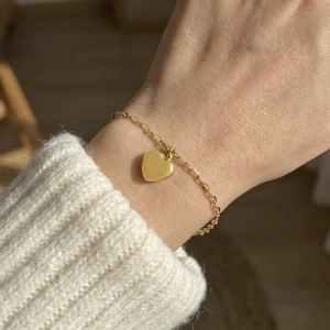 Gold-toned chic heart pendant bracelet worn over a cozy white knitted sweater sleeve