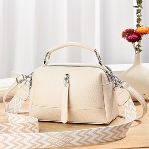 Chic beige lychee leather crossbody bag with patterned strap on wooden surface