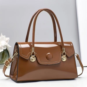 Detail of caramel brown patent leather handbag with gold fan-shaped hardware and a glossy finish