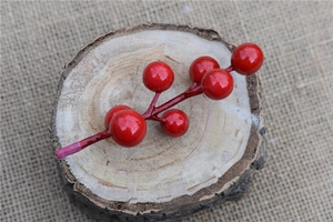 Close-up of bright red artificial berries on a rustic wooden stump for Christmas DIY decor