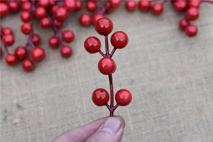 Close-up of hand holding artificial red foam berries for DIY Christmas tree decoration