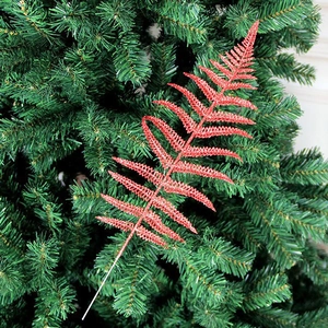 Dettaglio di foglia di felce rossa glitterata su sfondo verde di un albero di Natale