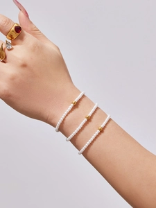 Detailed shot of triple-layered pearl beaded bracelets with golden metal accents and rings