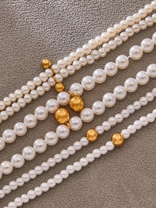 Macro shot of faux pearl necklaces with gold bead accents on gray textured fabric