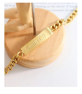 Macro detail of gold-plated cuban chain bracelet featuring a smile engraved square tag
