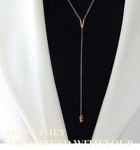 Dettaglio della collana a Y in oro rosa con lettere su abbigliamento bianco e nero