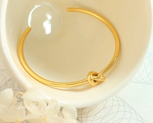 Dettaglio di un bracciale rigido dorato con nodo minimalista in una ciotola di ceramica