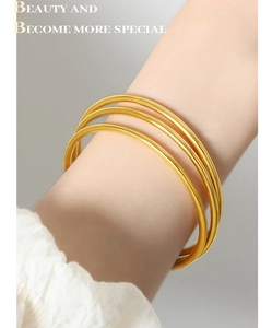 Close-up of three minimalist thin gold-plated titanium steel bangles on a woman wrist