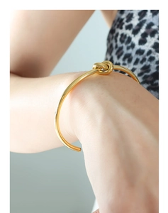 Dettaglio del bracciale rigido a nodo dorato lucido indossato sul polso femminile