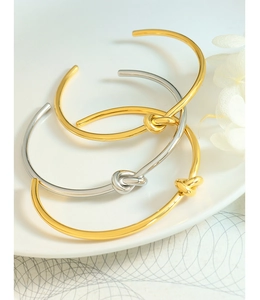 Dettaglio di bracciali con nodo lucido in oro e argento su un piatto bianco puro