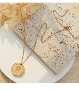 Detail of 18K gold-plated queen coin pendant necklace on decorative travertine stone