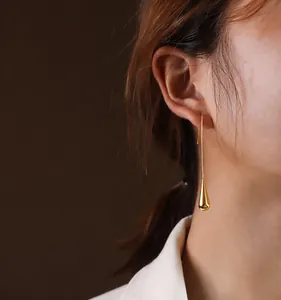 Macro view of long gold polished water drop earrings on model for a sleek aesthetic