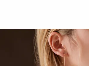 Detailed close-up of a long gold U-shaped earring worn by a model in soft lighting