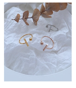 Three minimalist T-shape open rings in gold, silver and rose gold on white textured paper