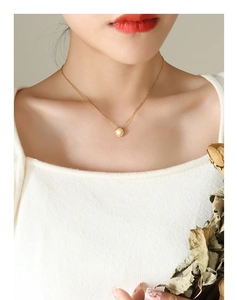Detail van elegante gouden ketting met ronde witte parelhanger op de nek van het model