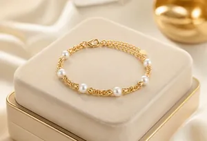 Detailansicht eines goldfarbenen Armbands mit weißen Perlen und einem Pfeil-Anhänger